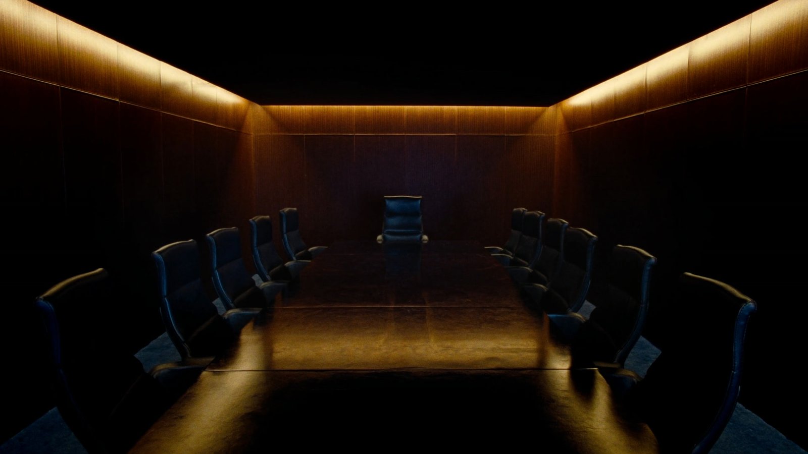 Sala de administração em madeira escura, com luz quente escondida no teto e cadeiras de direção frente a frente ao longo da mesa
